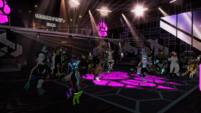 3rd person picture of PlaceHolder Club. The dance floor can be seen from the side of the stage. I'm dancing to the right of the picture, in front of the stage, with rainbow colors on me. About 30 avatars are visible, a few more are culled in the background. There were about 60 people in that moment.